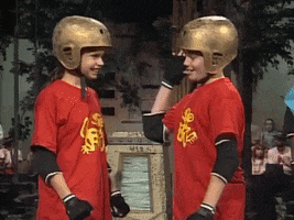 Reality TV gif. Two kids on Legends of the Hidden Temple stand next to each other with golden helmets on their heads. They high five and then pumps their fists with excitement.
