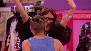 Reality TV gif. Two contestants from RuPaul's Drag Race are ecstatic and one throws their arms over the other's shoulders, pulling them into a big hug while jumping up and down.