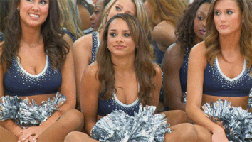 Video gif. A group of Dallas Cowboys cheerleaders clap and celebrate a cheerleader that sits among them. 