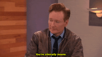 Late Night gif. Conan O’Brien sits down and looks at something with a serious expression and nods as he says, “You’re clinically insane.”