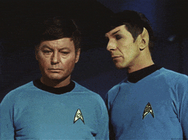 Star Trek gif. Leonard Nimoy and DeForest Kelley as Spock and Leonard McCoy stand next to each other in their matching blue uniforms. Spock turns and walks off while McCoy rolls his eyes in annoyance.