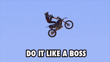 Sports gif. Motocross rider is in the midst of flying through the air and stands up on his bike, putting one foot on the handlebars. Text, "Do it like a boss."