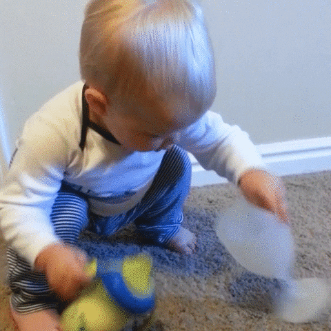 Video gif. Baby places his sippy cup inside of a plastic wine glass, then picks it up and drinks from it.