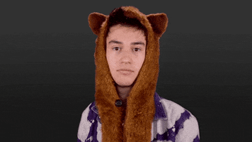Video gif. Jacob Collier, wearing an orange furry hat with animal ears, shrugs with an unimpressed expression.
