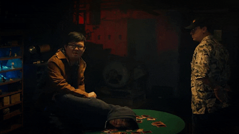 Two guys playing the Yu-Gi-Oh card game in a dark room. One man flips over the green table and the cards slide off.