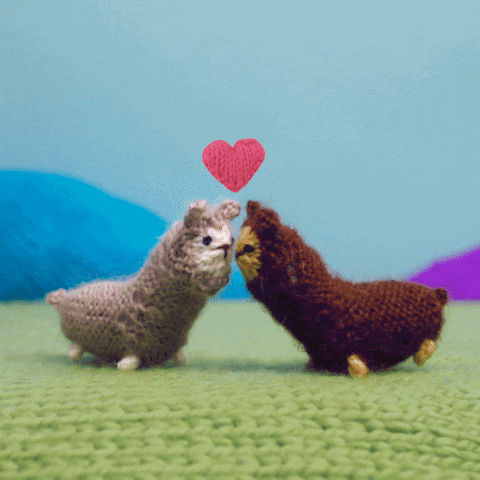 Stop-motion gif. Knitted scene with a gray alpaca and a brown alpaca who turn to face each other and kiss, as pink knitted hearts fly up between them.