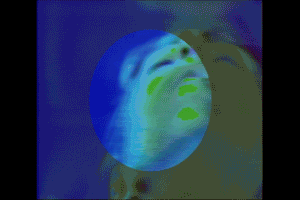 Video gif. Closeup moving closer on a person's upturned face as they put their hands over their cheeks and eyes. The video is very low quality, with a superimposed circle over the center, and the image flickers. It's blue and green in either a trippy, psychedelic, or low-fi way. 