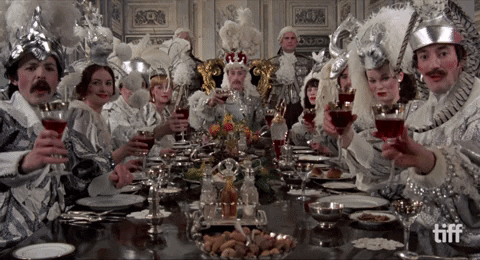 Gif s lidmi sedícími u stolu a připíjejícími si vínem ve stříbrných kostýmech. 