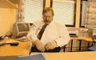 Video gif. Man sits behind an office desk and haphazardly tosses papers and folders up in the air angrily before leaning back in his chair and crossing his arms.