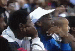 Sports gif. Sitting on the sidelines of an NBA game, a shocked Michael Jordan’s jaw drops, and he raises his hands above his head in excitement.