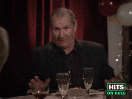 Sponsored GIF. Ed Harris sits at a party table where this some awkard tenstion. He attempts to reassure while nodding and saying to the other dinner guests at the table, "I'm having a great time tonight."