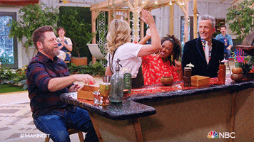 Reality TV gif. Nick Offerman, Amy Poehler, Dayna Isom Johnson, and Simon Doonan on Making It sitting at a bar, high-fiving each other and cheering.