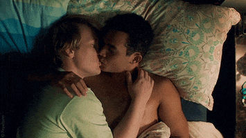 TV gif. Adam Faison and Josh Thomas as Alex and Nicholas from Everything's Going to Be Okay lay in bed and kiss tenderly.