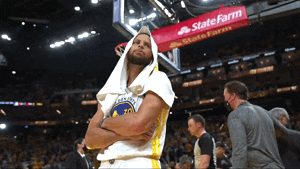 Sports gif. Stephen Curry of the Golden State Warriors has a towel over his head and his arms crossed. He nods his head once and gives a crooked, confident smile.