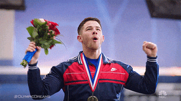 TV gif. Nick Jonas, dressed as an Olympian, wears a medal around his neck and raises his arms to the sky in victory, his mouth open in a "wooo!" shape. He's obviously just won an Olympic medal for being the cutest Jonas Brother.